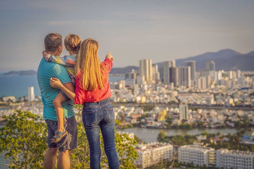 A family of three looks out over the high-rise skyline and coastline of Nha Trang from a hilltop viewpoint, a popular beach city for traveling with children in Vietnam.