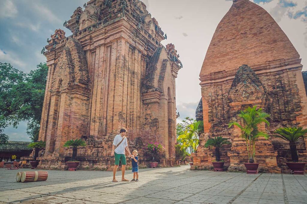 A father and his small son hold hands in front of the tall brick Cham towers of Po Nagar in Nha Trang, an interesting historical stop when traveling with children.