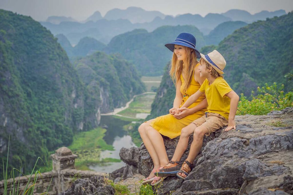 A mother and her son sit on the rocks at the Mua Cave viewpoint in Ninh Binh, looking out over the winding river and green karst valley, a rewarding short climb when visiting Vietnam with kids.