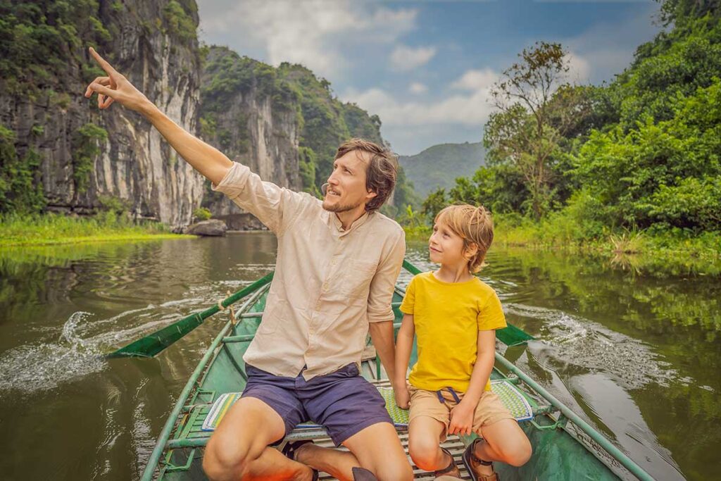 A father points out the scenery to his son during a rowing boat trip through the karst landscape of Trang An in Ninh Binh, one of the best activities when traveling with children in Vietnam.