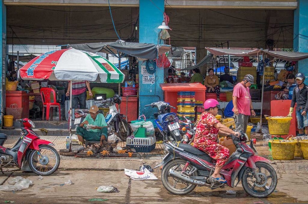 Busy Ha Tien market entrance with motorbikes, vendors, and seafood stalls.
