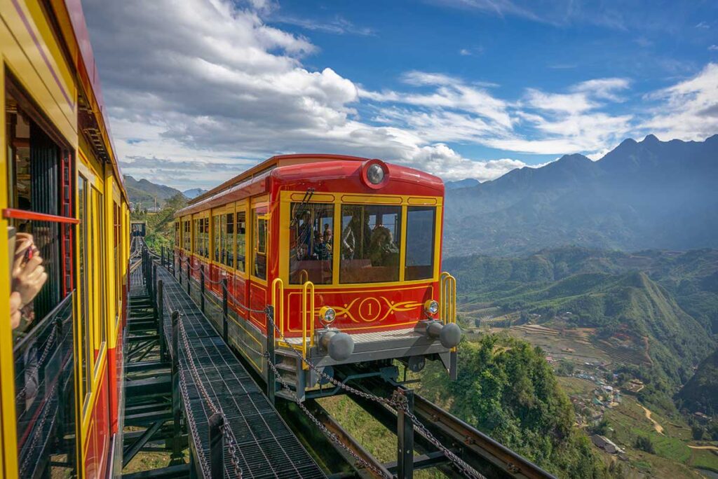 A bright red and yellow mountain train climbs along the track high above the green valley near Sapa, a short and scenic ride that works well on a holiday in Vietnam with kids.