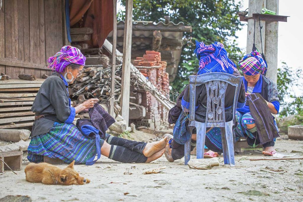 Local ethnic woman in traditional clothes are sitting in front of a house in a village  in Mu Cang Chai district