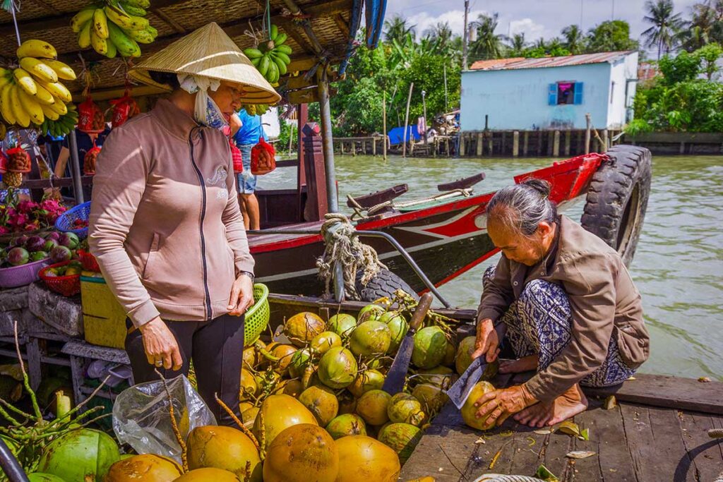 Floating market vendors in My Tho, Mekong Delta, selling coconuts and tropical fruit directly from boats on the river.