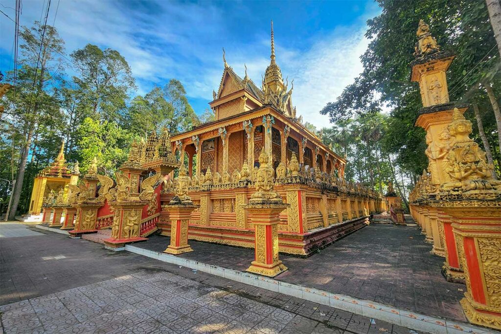 Phu Ly Khmer Pagoda in Vinh Long, Vietnam, featuring golden walls, ornate carvings, and traditional Khmer architecture surrounded by trees.