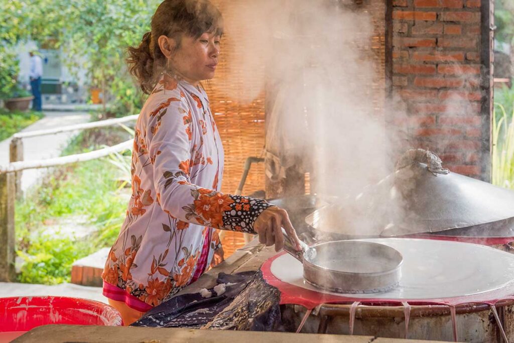 Local woman making rice paper over steaming pot at a family workshop in Can Tho, Vietnam