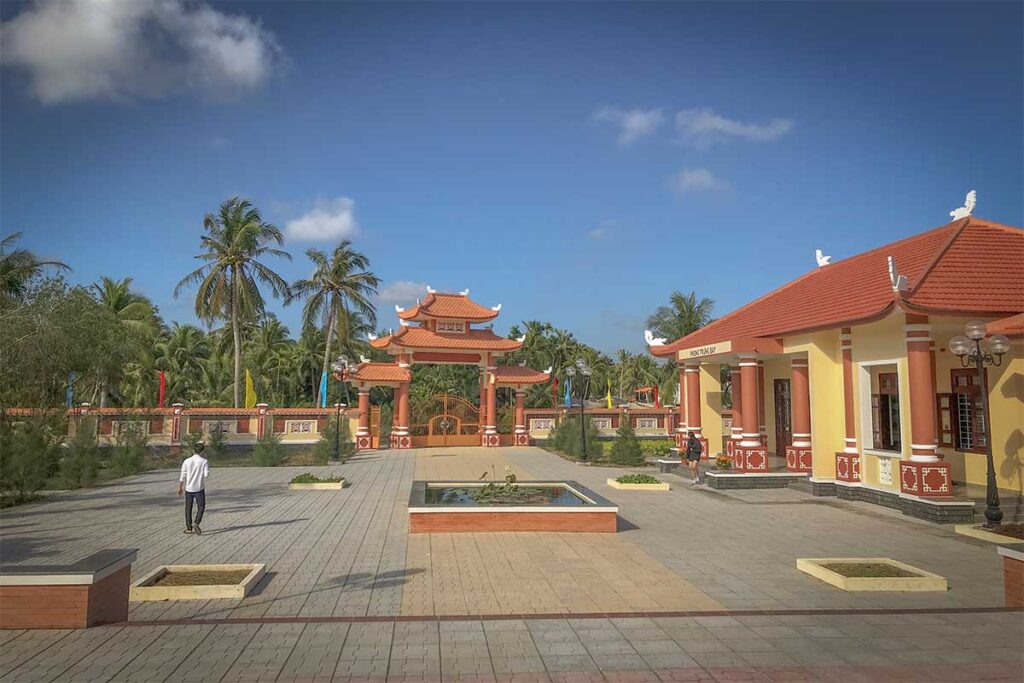 Tuyen Linh Temple courtyard in Ben Tre – View of the temple grounds with traditional Vietnamese gate, tiled roofs, and palm trees in the background.