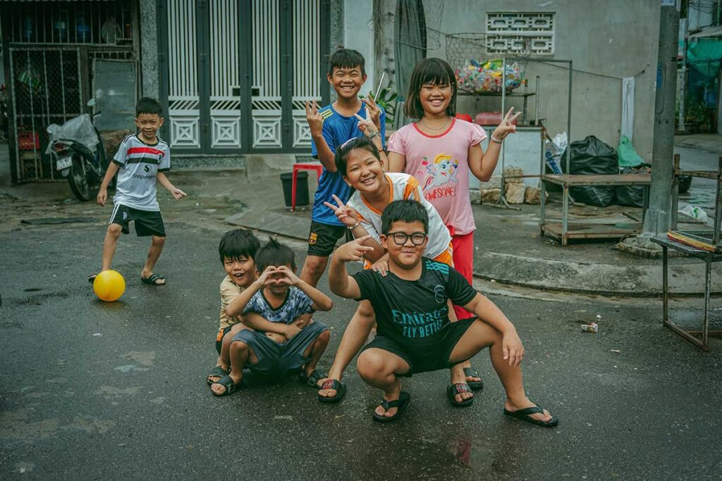 A group of cheerful Vietnamese children play and pose together on a quiet residential street, a glimpse of everyday local life families often notice when traveling in Vietnam with kids.