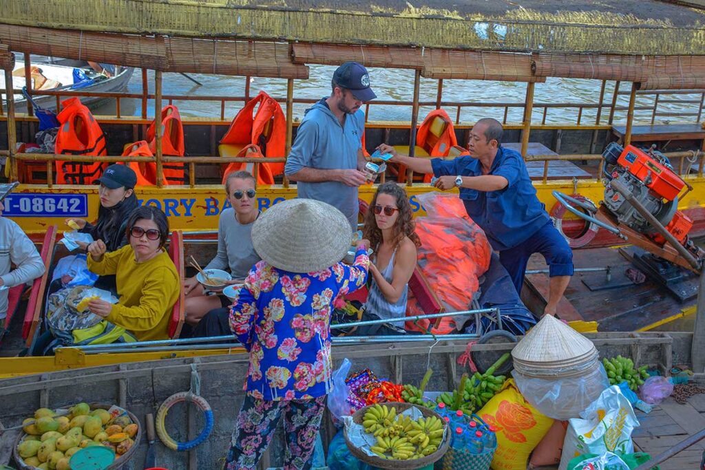 Tourists on a boat at Phong Dien Floating Market buying fruit and snacks from local vendors in Can Tho.