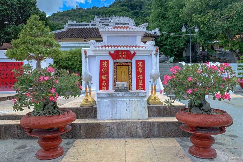 Thoai Ngoc Hau Tomb on Sam Mountain, Chau Doc, with white shrine, red calligraphy, and flowering bonsai trees.