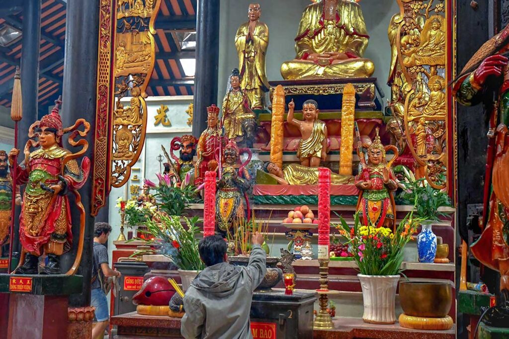 Interior of Tay An Pagoda in Chau Doc with golden Buddha statues, wooden carvings, and worshippers offering incense.