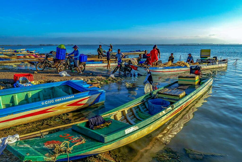 Locals on small wooden fishing boats on the shores of Dau Tieng Lake