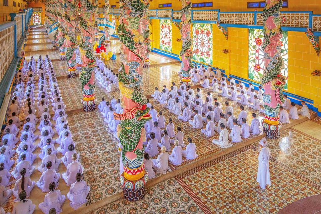 People in white ropes sitting inside Tay Ninh Holy See Cao Dai Temple during praying times
