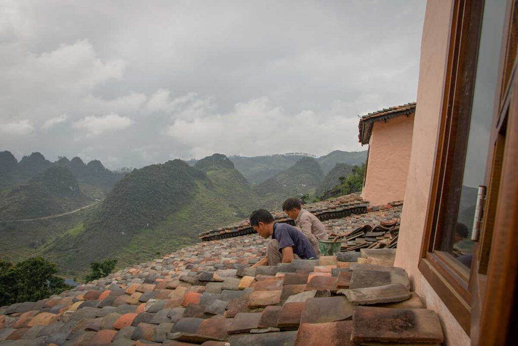Local builders installing traditional stone roof tiles overlooking the karst mountains of Ha Giang, ensuring the lodge blends naturally with regional architecture.