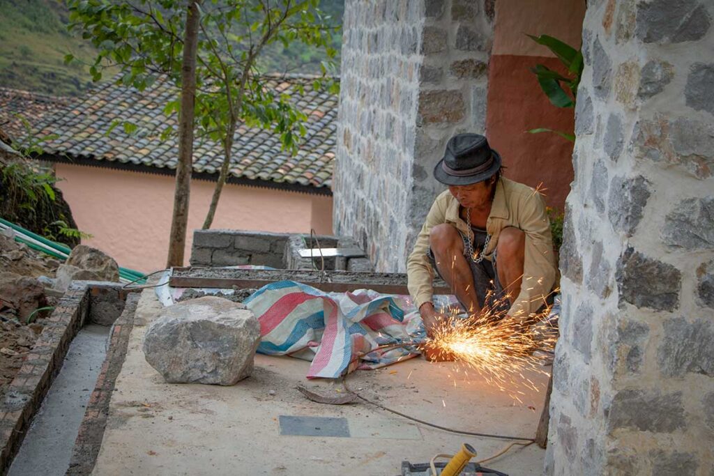 A local craftsman welding metal components during the final construction phase of Local Vietnam’s Ha Giang lodge, using traditional stone architecture.