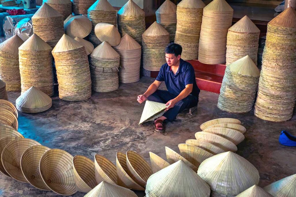 a man holding a conical hats at a warehouse full of conical hats at Chuong Village near Hanoi