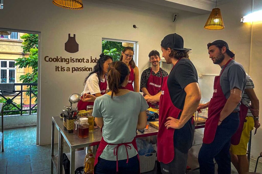 Hanoi Apron Up Cooking Class: Tourists wearing aprons gather around a kitchen table, learning to prepare traditional Vietnamese dishes at Hanoi Apron Up Cooking Class.