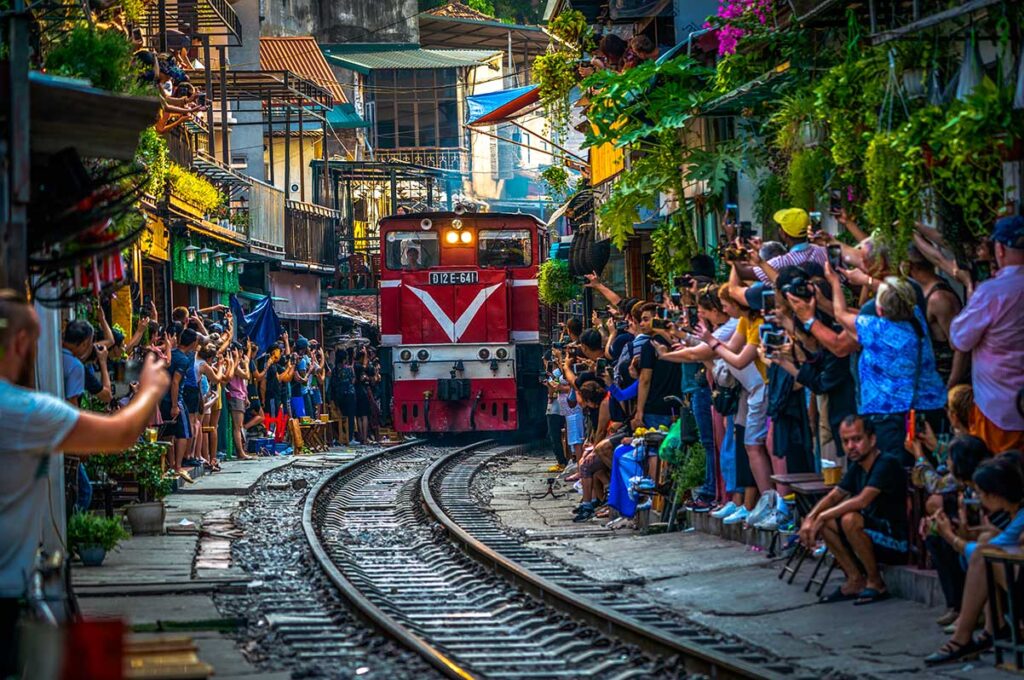 Hanoi Train Street with lots of tourists making photos of the incoming train through a narrow street with train track