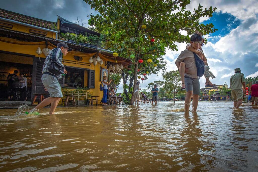 Tourist carrying his girlfriend through an ankle-deep flooded street in Hoi An after a heavy rain during Vietnam's rainy season.