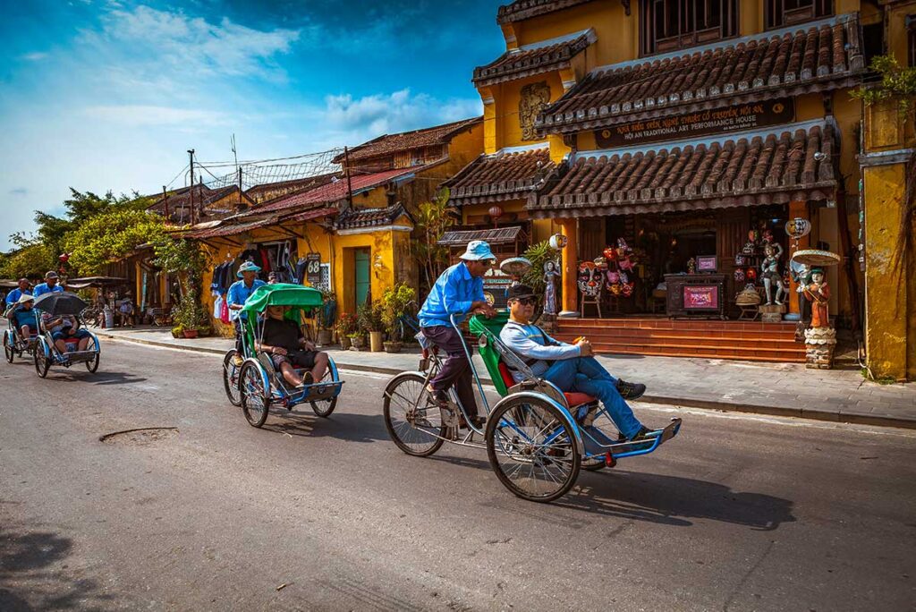 Cyclo Ride in Hoi An: Tourists enjoy a leisurely cyclo ride through the charming yellow shophouses of Hoi An's ancient town.