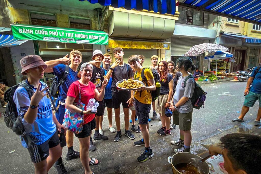 Chef Duyen's Home Cooking Class Street Food Tour: Tourists sample delicious street food from a local vendor as part of Chef Duyen's immersive cooking class experience in Hanoi. (