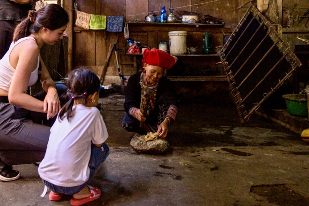 a tourist woman sitting with her kid in a homestay in Sapa watching a ethnic minority woman preparing a meal on traditional ways
