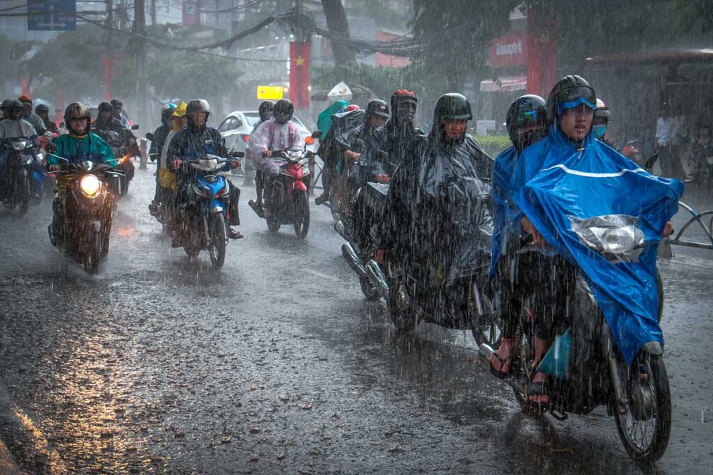 Motorbikes navigating through pouring rain with rain ponchos during Vietnam's rainy season.