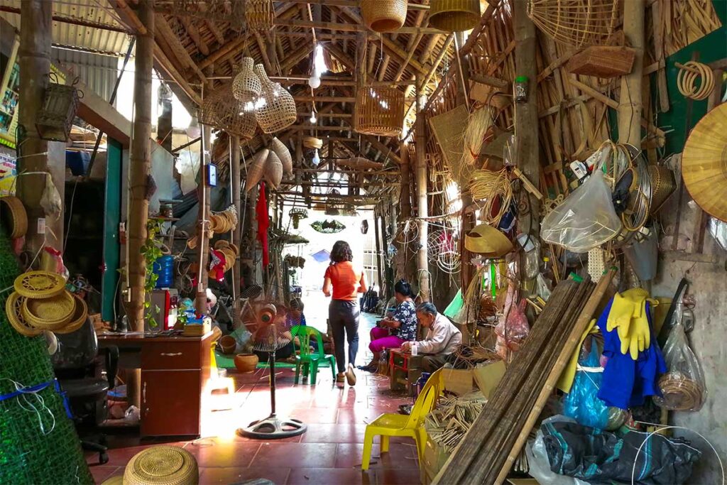 A narrow street in Phu Vinh Bamboo Village, lined with stalls selling colorful bamboo and rattan crafts.