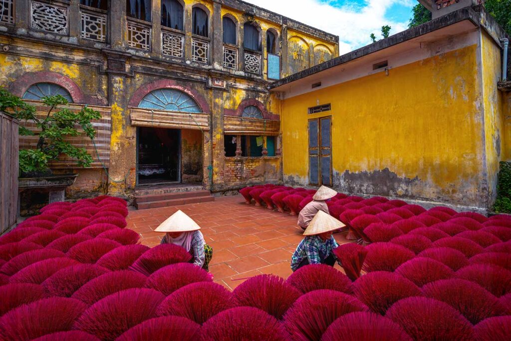 three woman sitting between a field of incense sticks at Quang Phu Cau Incense Village