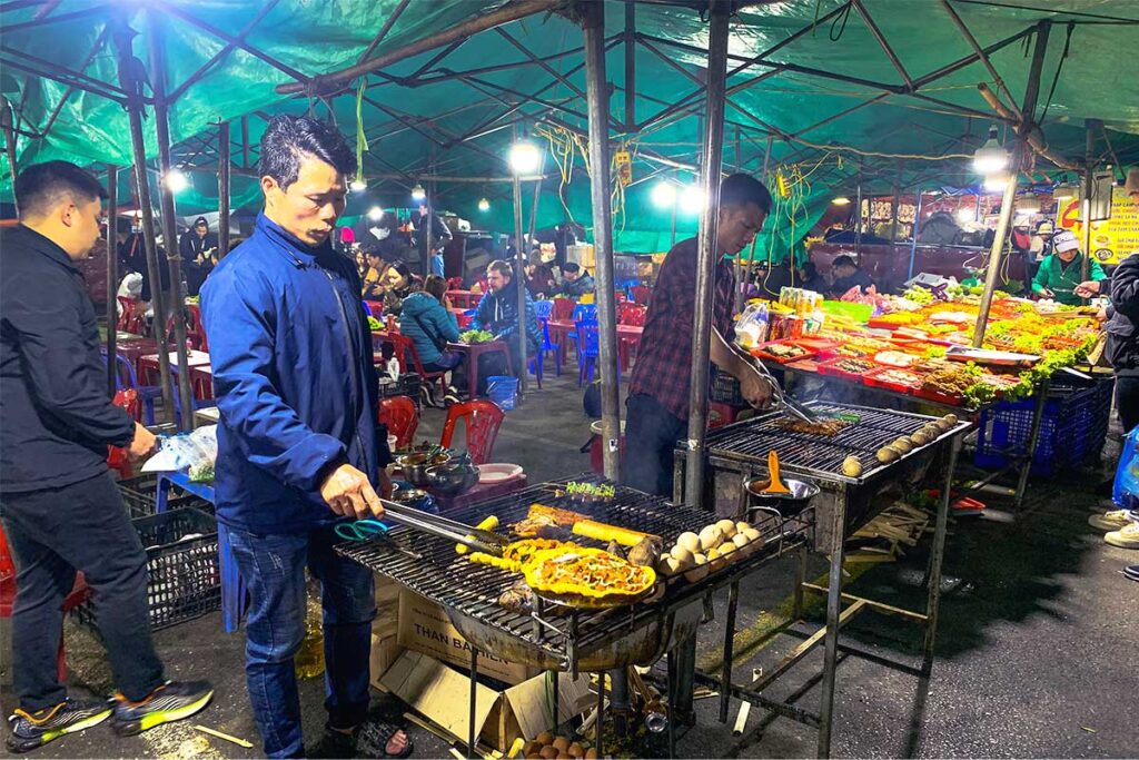 a local man cooking street food on a grill at the night market in Sapa