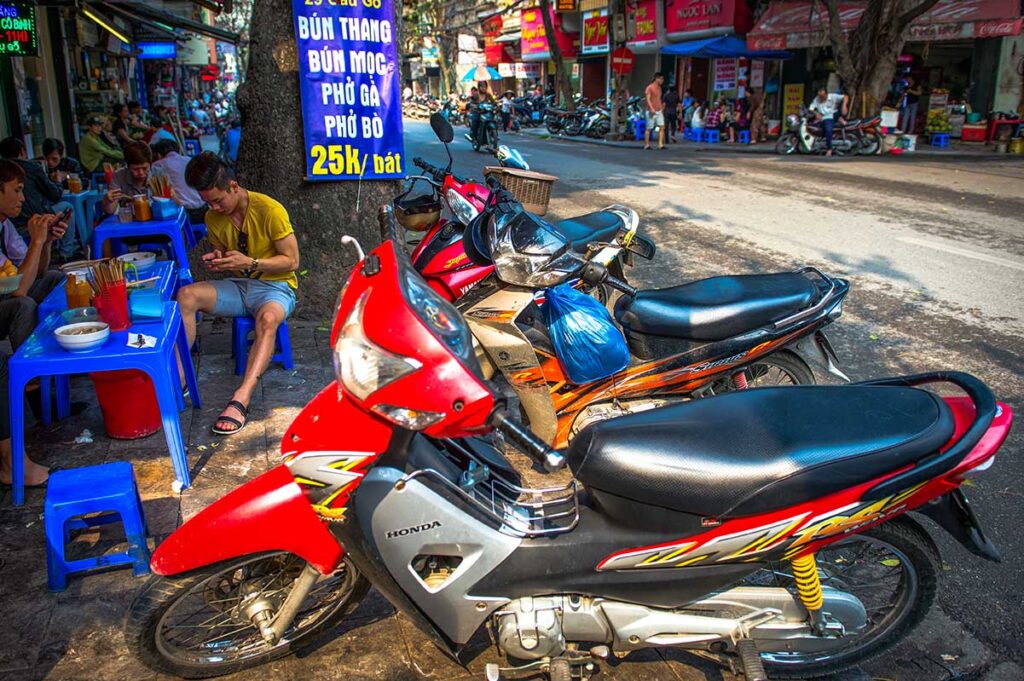 Sidewalk in Vietnam filled with motorbike parking and bustling street food vendors.