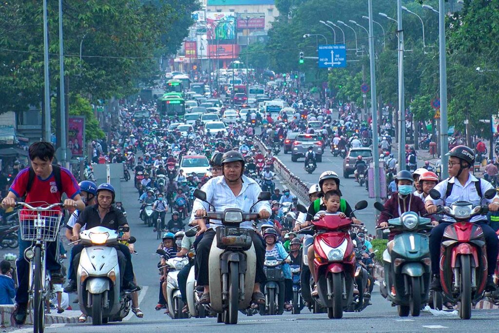 Extremely busy traffic scene in Vietnam with a sea of motorbikes, alongside cars and buses.