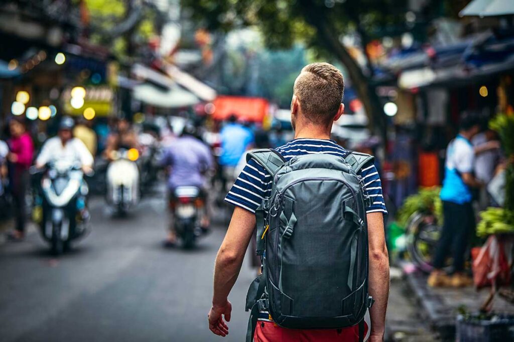 Male solo traveler with a backpack walking through the vibrant streets of Hanoi Old Quarter.