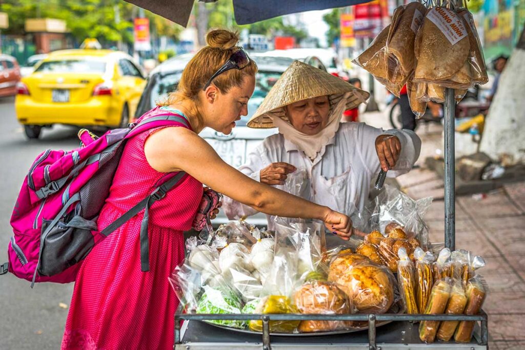 Solo female traveler at a bustling street food vendor in Hanoi, pointing to her food choice.