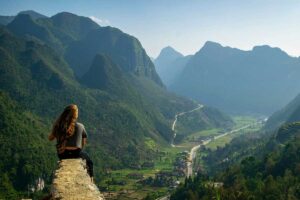 Solo female traveler sitting on a rock, admiring the stunning valley views in Ha Giang, Vietnam.