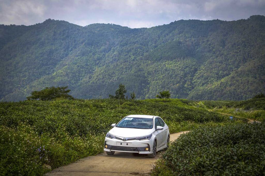 A car in Cao Bang that is rented including a driver for sightseeing in the province is driving over a small road with Cao Bang's mountains on the background