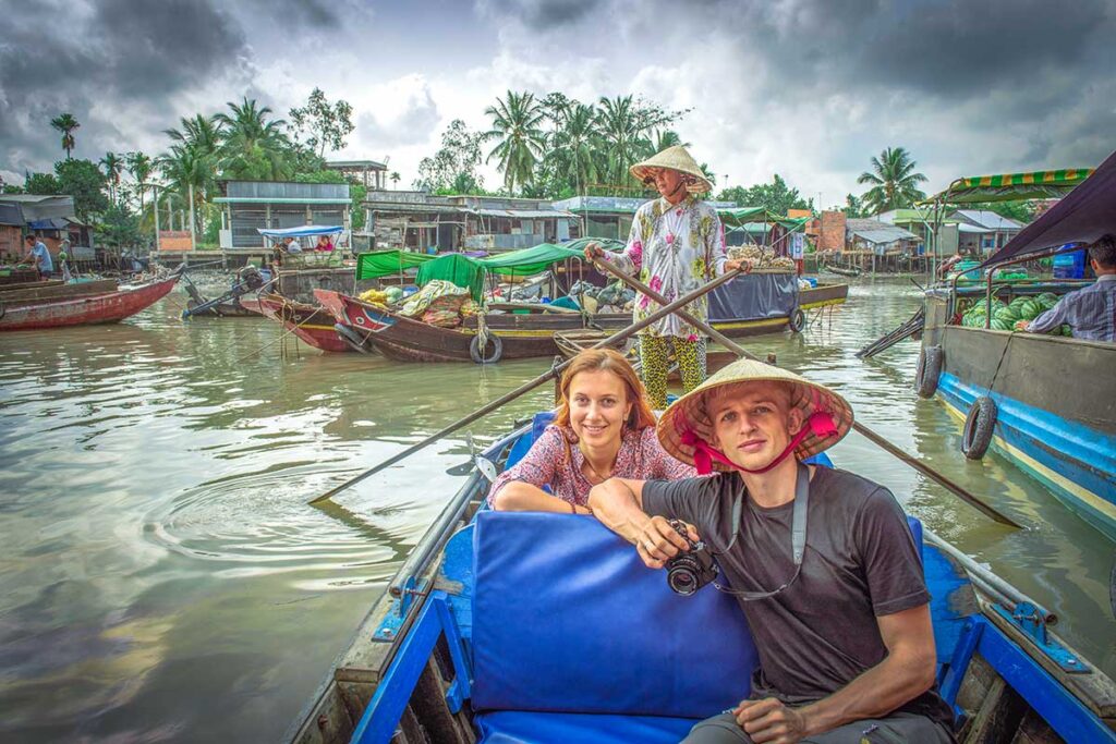 A tourist couple sitting in a traditional rowing boat while going through the canals of the Mekong Delta