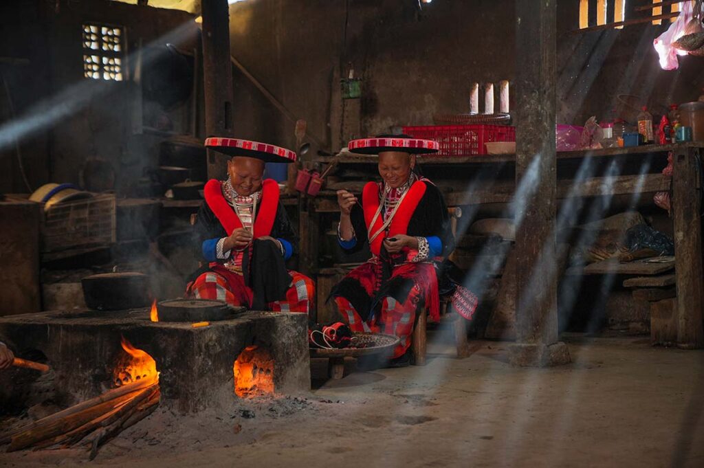 Two Red Dao ethnic minority woman inside a house cooking on an open fire in Cao Bang