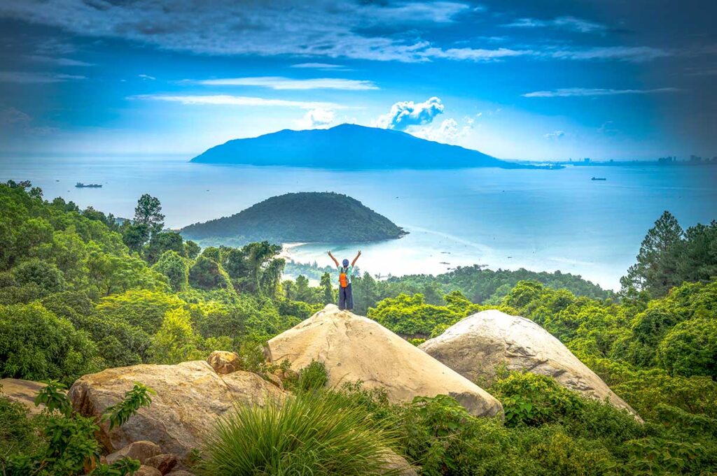 A tourist standing in the distance on a huge rock, overlooking the Hai Van Pass viewpoint with stunning coastal views - Vietnam nature