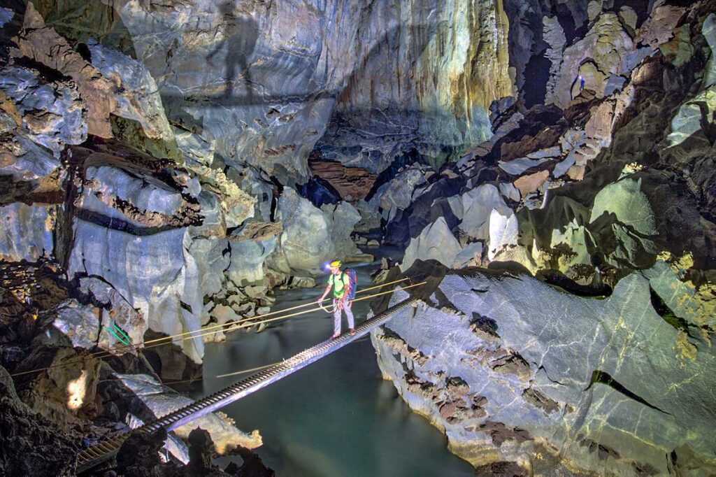 A man crossing a beam over an underground river inside Hang Son Doong Cave