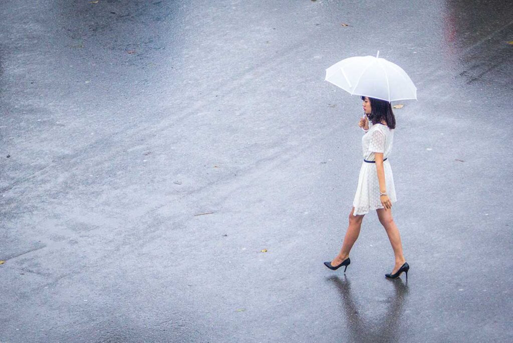 A well dresses Vietnamese woman crossing the street with an umbrella in the rain in Hanoi