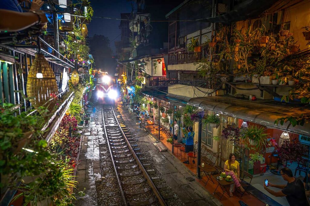 People sitting in a coffee shop along Hanoi Train Street during the rain with a train coming from a distance