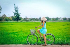 A traveller with conical hat on a bicycle is looking at the green rice fields during a countryside cycling ride around Hoi An