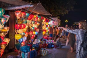 Colorful lantern stalls at Hoi An Night Market with travelers browsing handmade souvenirs and glowing lanterns after dark.