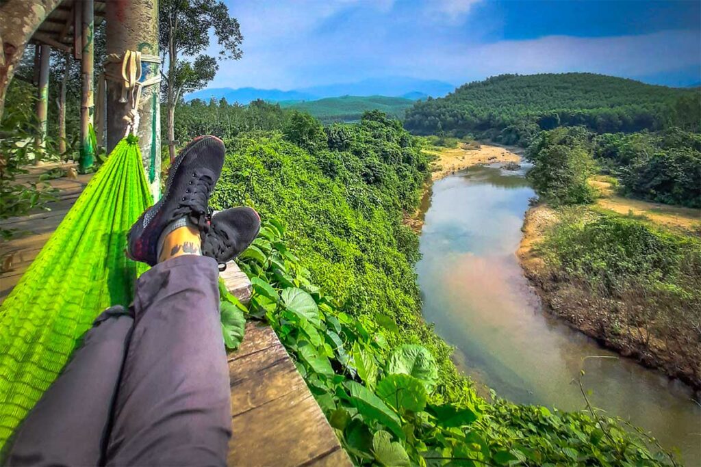 A traveler laying in a hammock with stunning view of forest, a river and mountains at Cuong Rung Farm