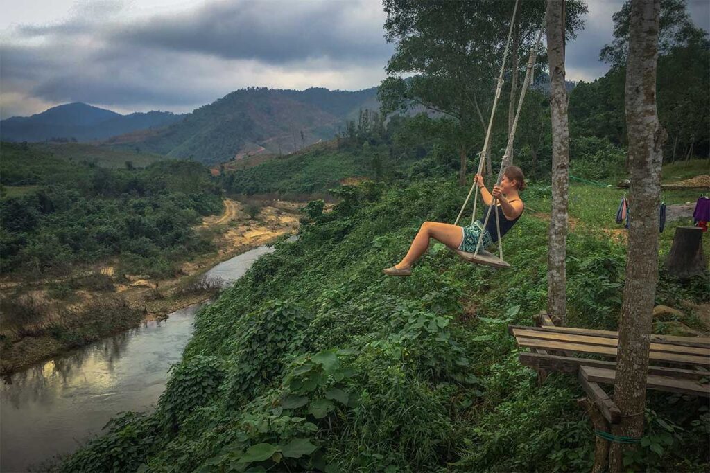 A travelers is swinging on a swing on top of a mountain with amazing views over the river below and forest and mountains around it at Cuong Rung Farm