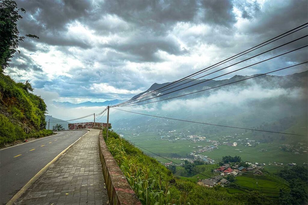 An empty Muong Hoa Road with on the right side stunning views of mountains and rice fields of Muong Hoa Valley in Sapa