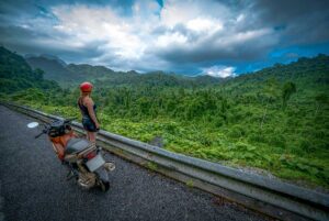 A tourist standing next to her motorbike on the road overlooking the epic jungle landscape of Phong Nha National Park - One of the best destinations to see nature in Vietnam