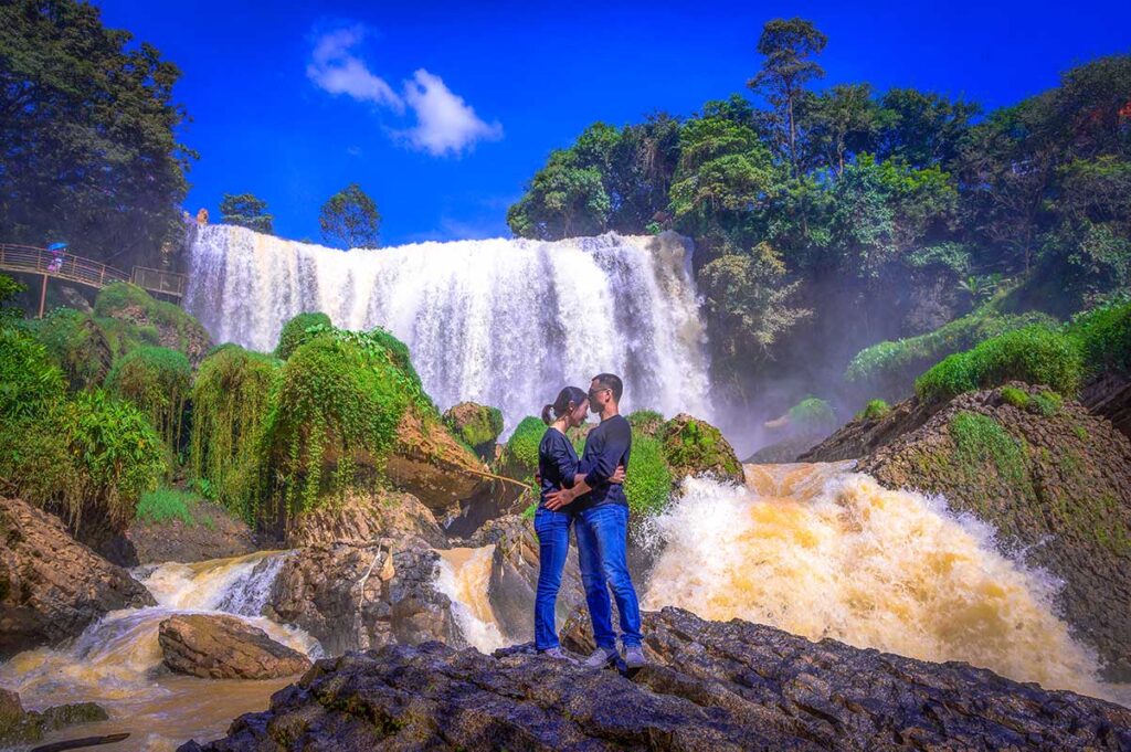 A romantic couple kissing each other in front of the Elephant waterfall in Dalat