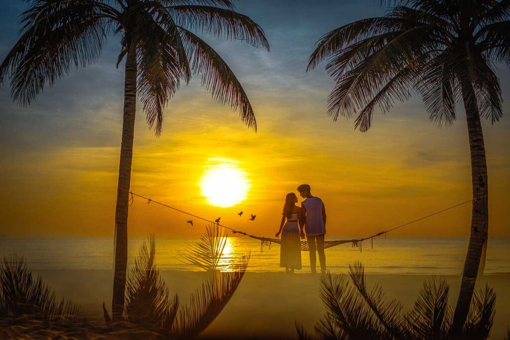 A romantic couple sitting on a hammock on the beach of Phu Quoc while watching the sunset